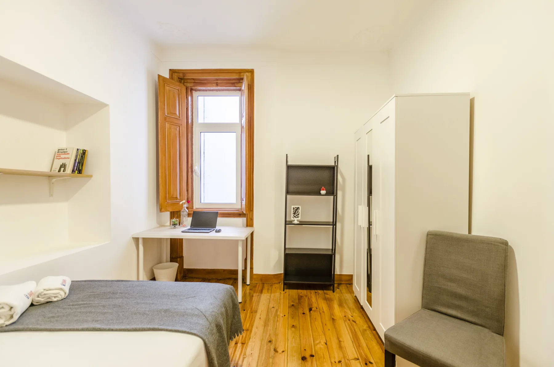 Un dormitorio con una cama, un escritorio bajo la ventana y una silla.