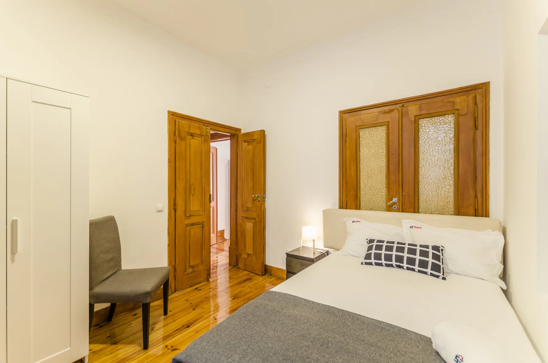 Un dormitorio con una cama, asiento gris y puertas de madera.