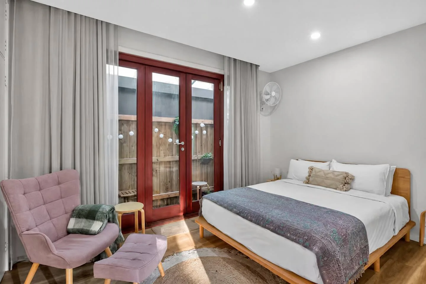 A bedroom with a bed, a lounge chair, and glass doors opening onto a fenced outdoor area.