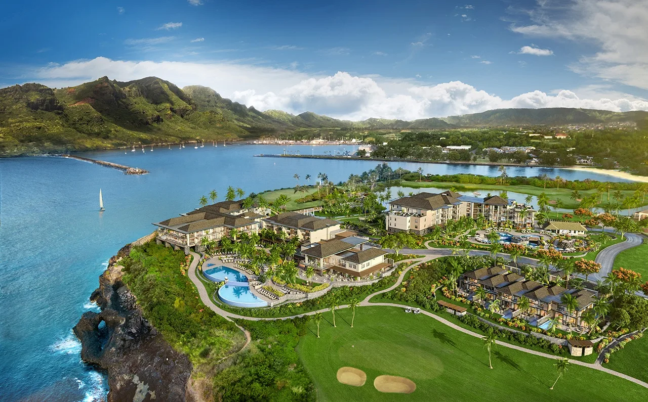 Aerial view of a coastal resort complex beside a blue bay and green hills.