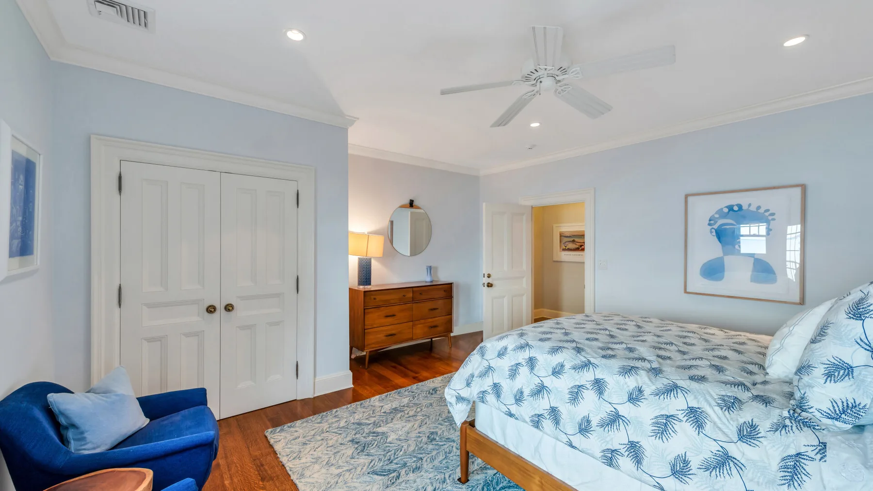 Un dormitorio con una cama estampada, una cómoda de madera y asientos azules.