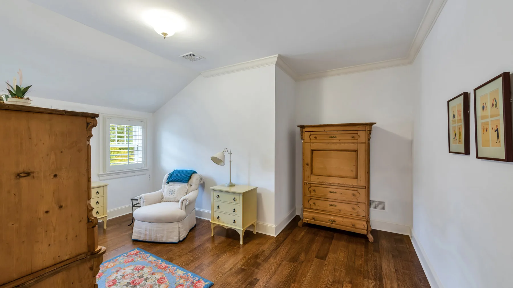 Una zona de estar en un dormitorio con un sillón acolchado, muebles de madera y una alfombra colorida.