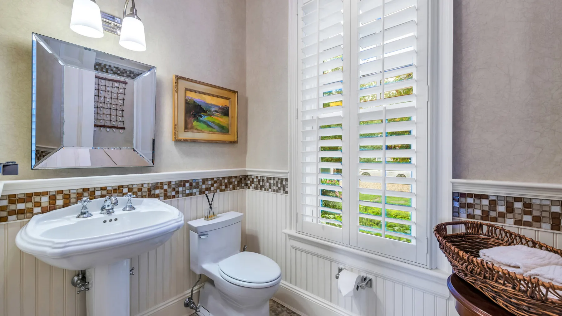 Un baño con lavabo de pedestal, inodoro y una ventana con contraventanas blancas.