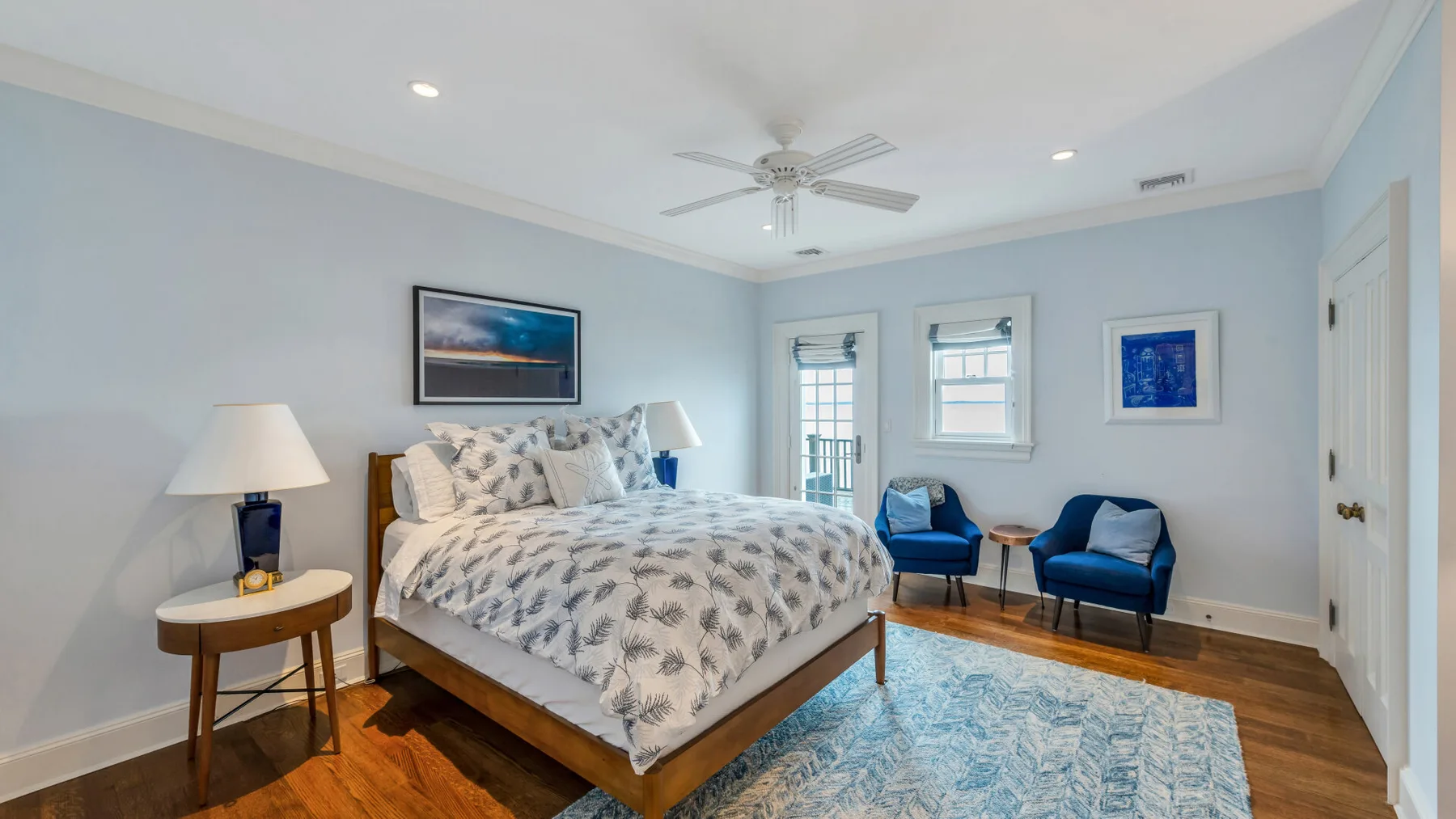 Un dormitorio luminoso con una cama grande, dos sillones azules y una alfombra estampada.