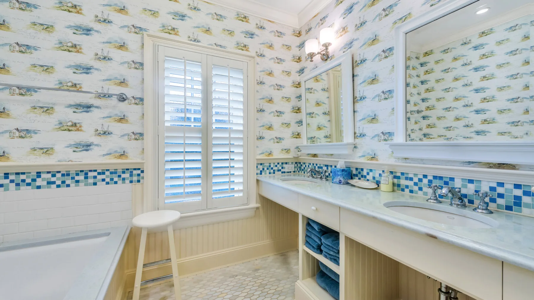 Un baño con bañera, lavabo doble y una ventana con contraventanas.