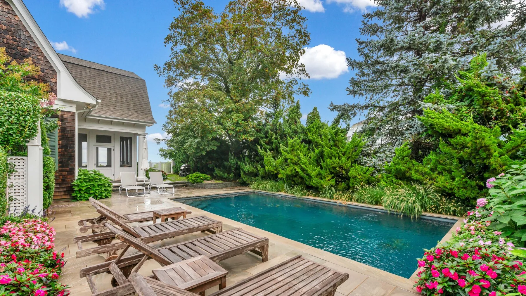 Una piscina al aire libre junto a una casa, con tumbonas y plantas con flores.