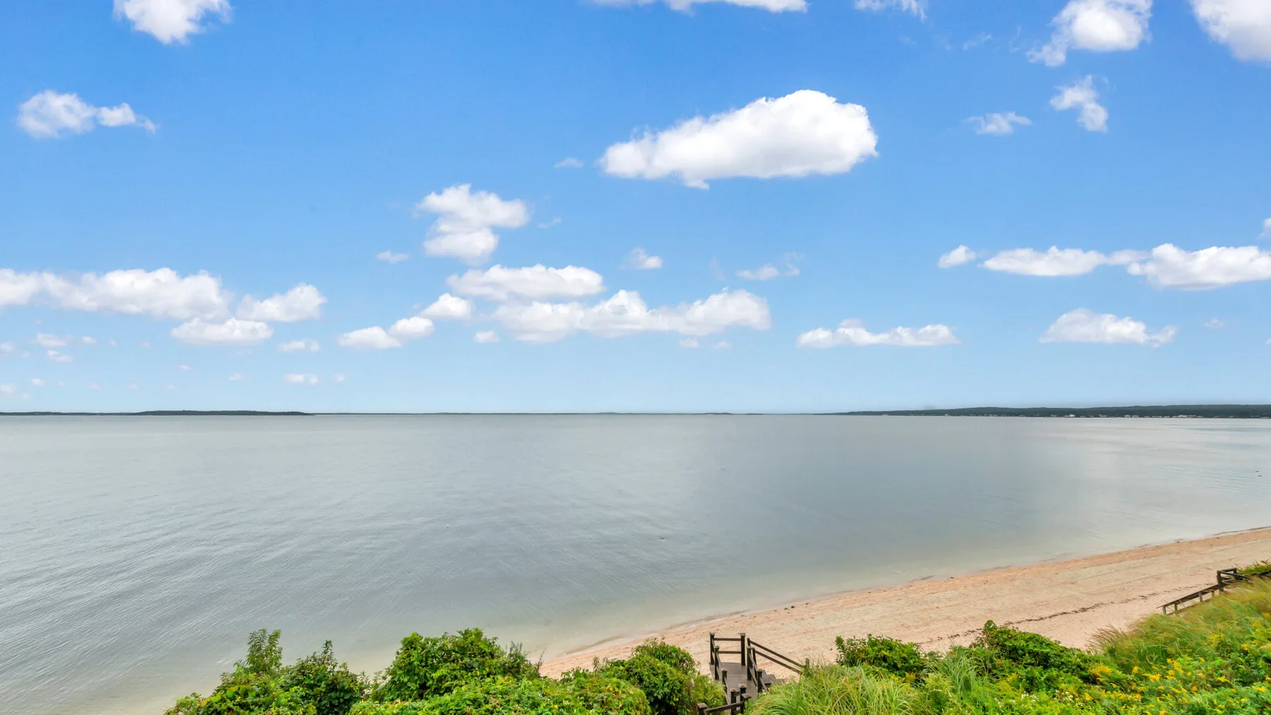 A sandy beach meets calm water beneath a bright, cloudy sky.