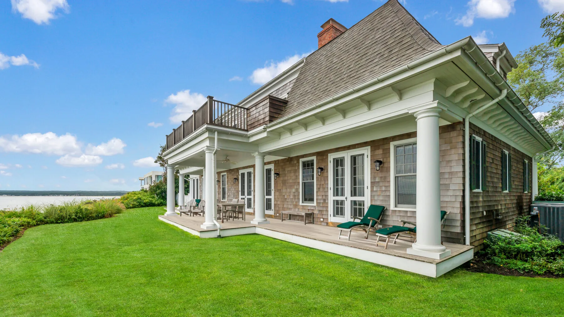 A large house with a covered patio, lawn, and water visible beyond the yard.