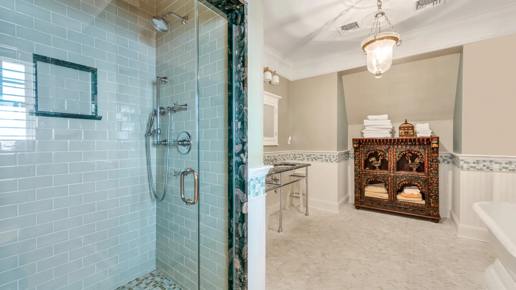 Una ducha con azulejos da a un baño con un mueble decorativo.