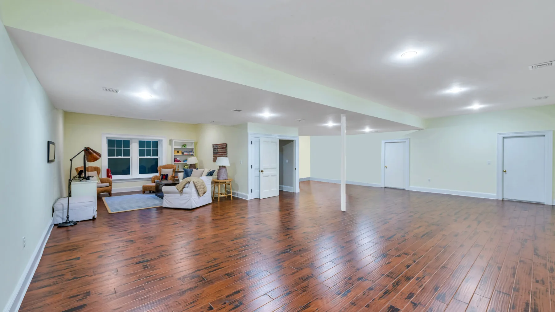Una habitación amplia con suelo de madera pulida y una pequeña zona de estar junto a las ventanas.