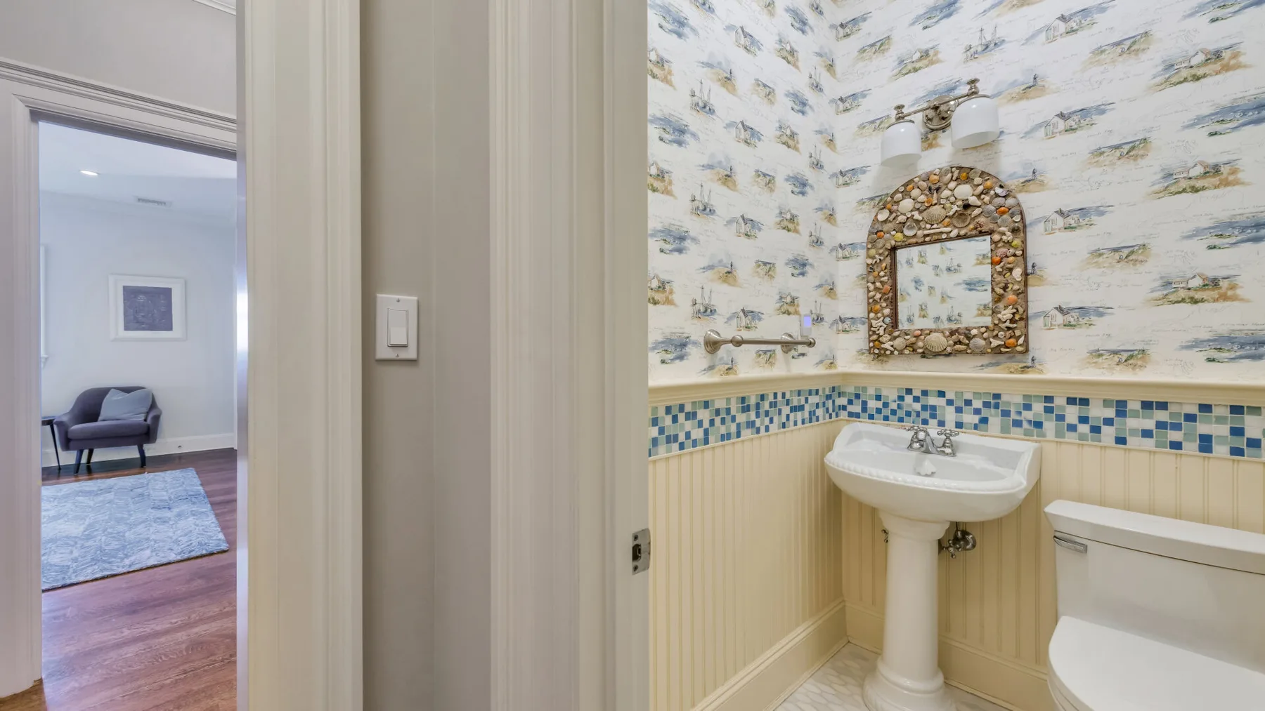 Un baño con lavabo de pedestal, inodoro y papel tapiz estampado.
