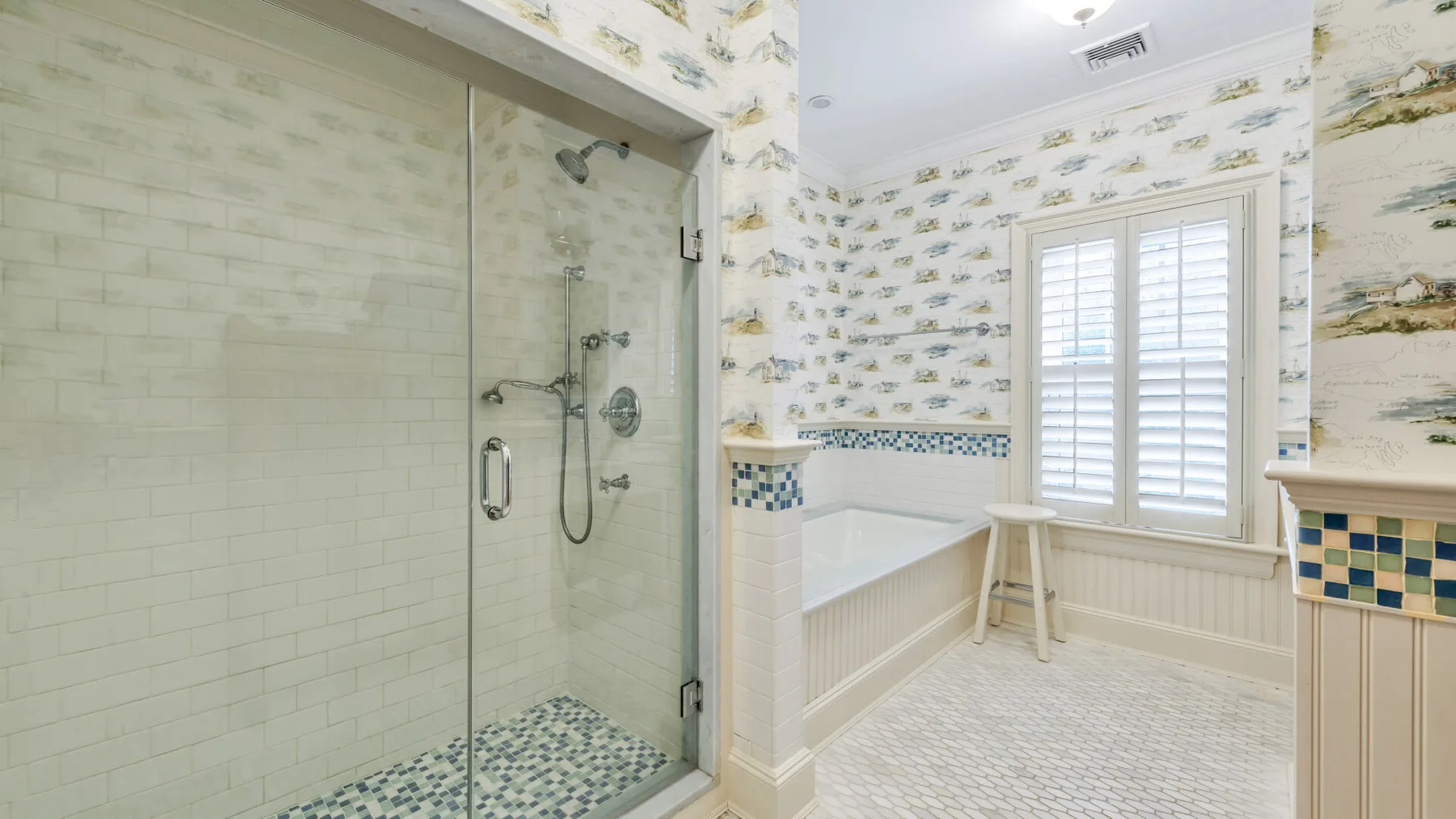 Un baño luminoso con ducha de vidrio, bañera y ventana con contraventanas.