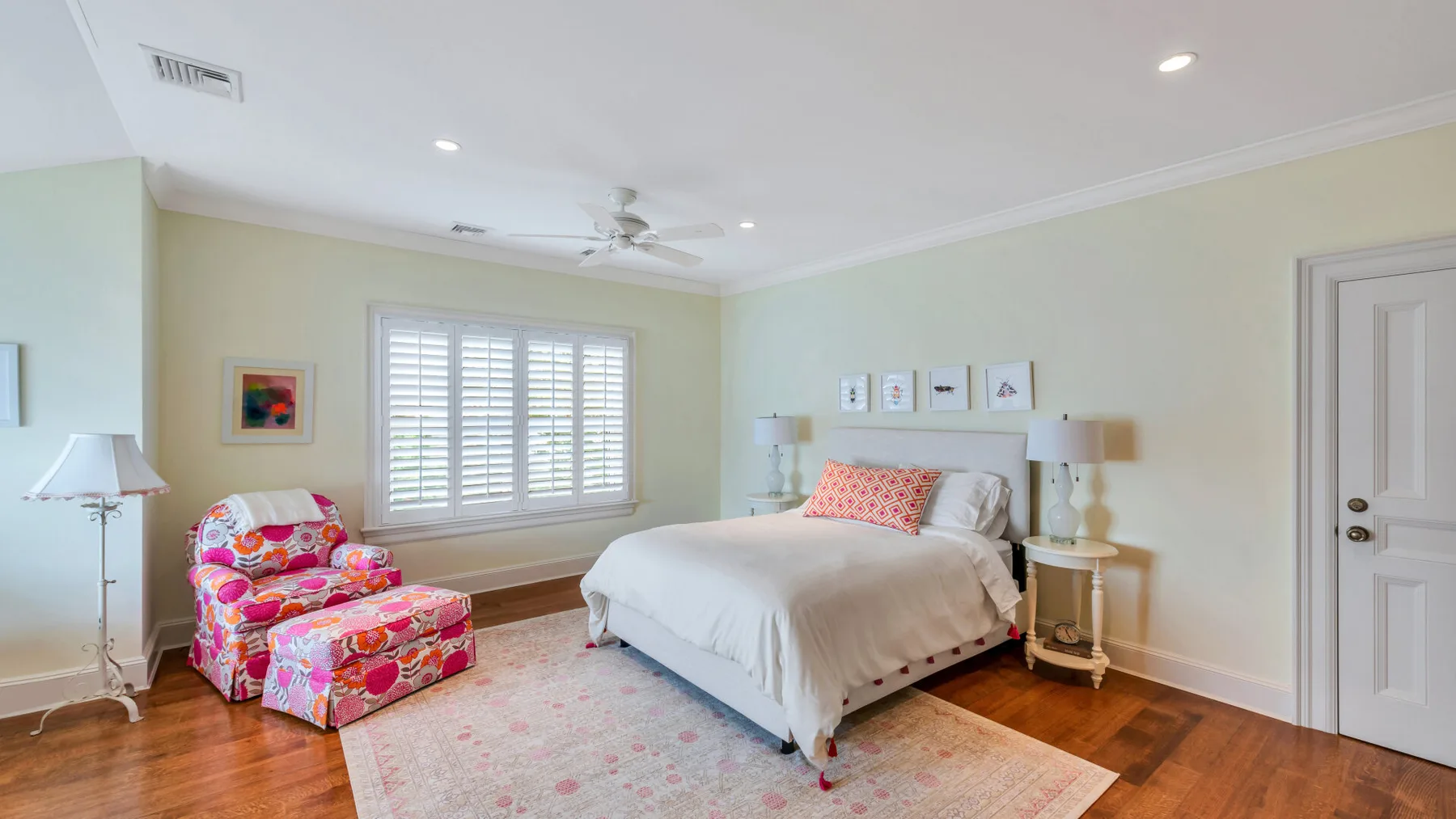 Un dormitorio con una cama, asientos coloridos y una gran ventana con contraventanas.