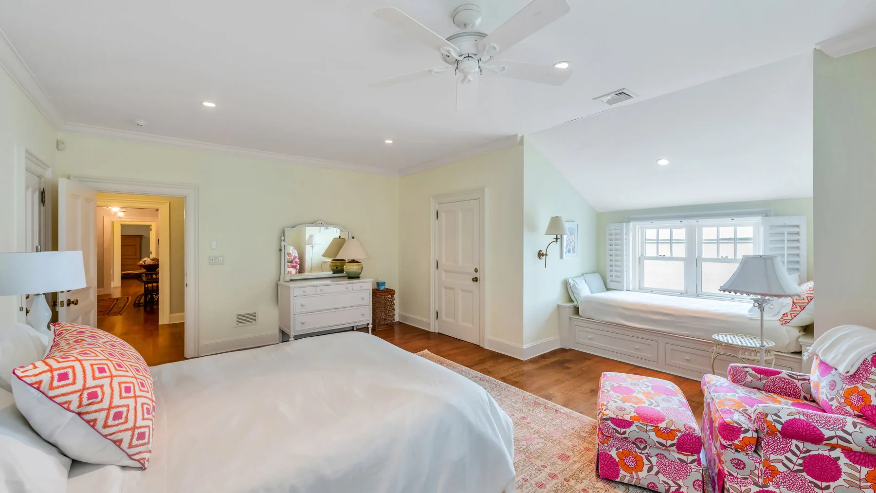 Un dormitorio con cama, cómoda y asientos junto a un rincón luminoso con ventana.