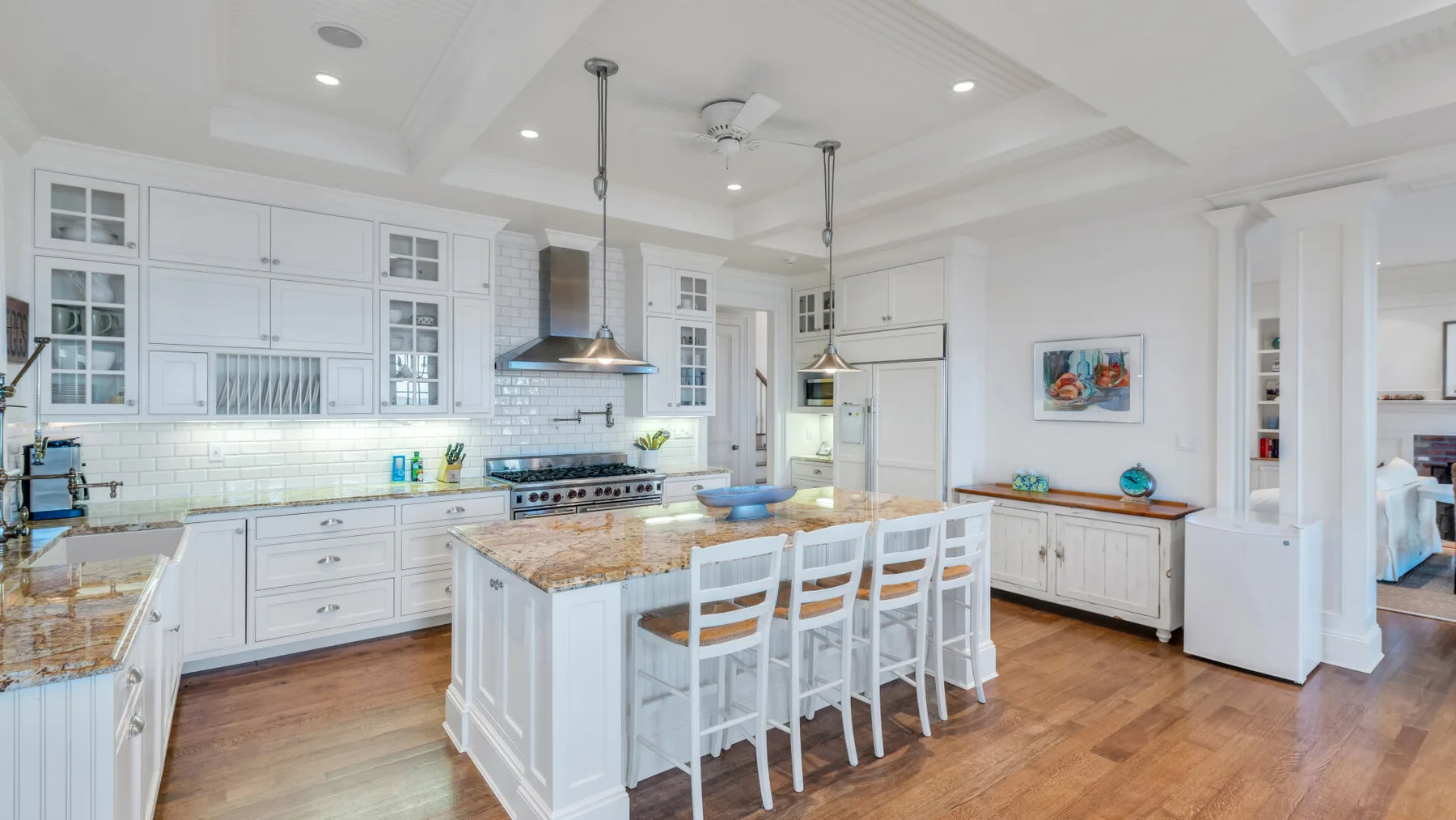 Una cocina luminosa con gabinetes blancos, una isla central y piso de madera.