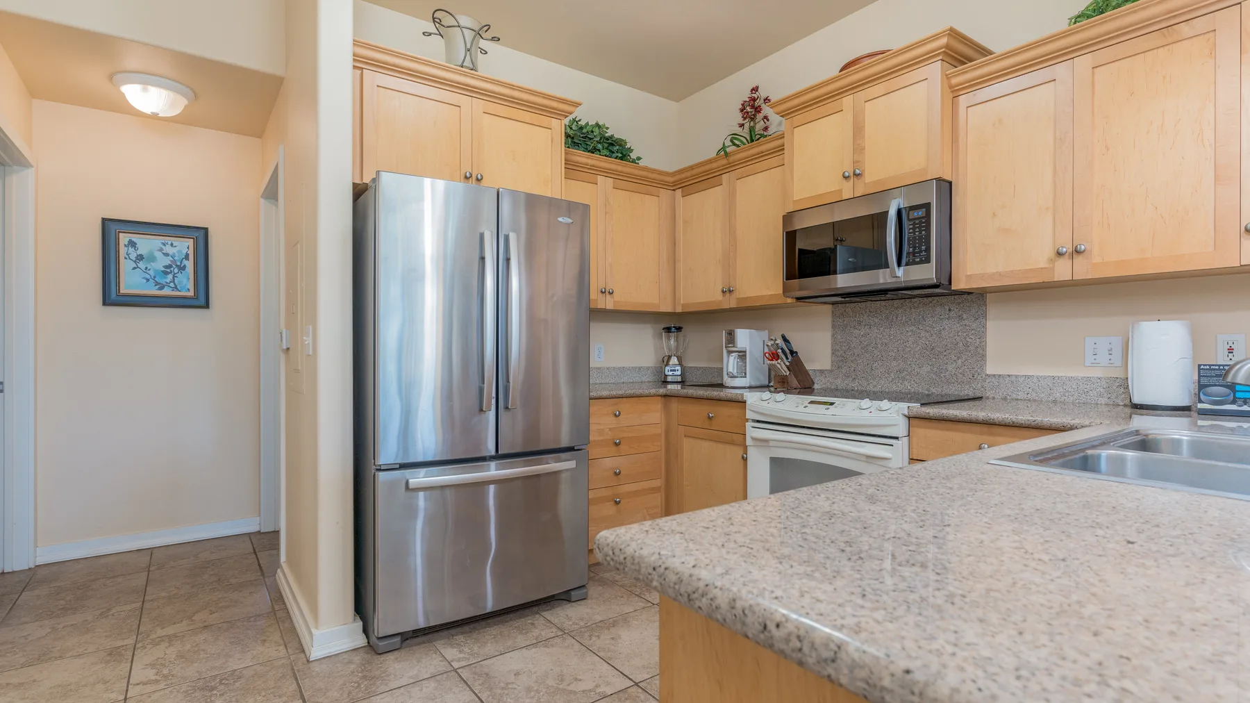 A bright kitchen with light wood cabinets, stainless steel appliances, and a stone countertop.
