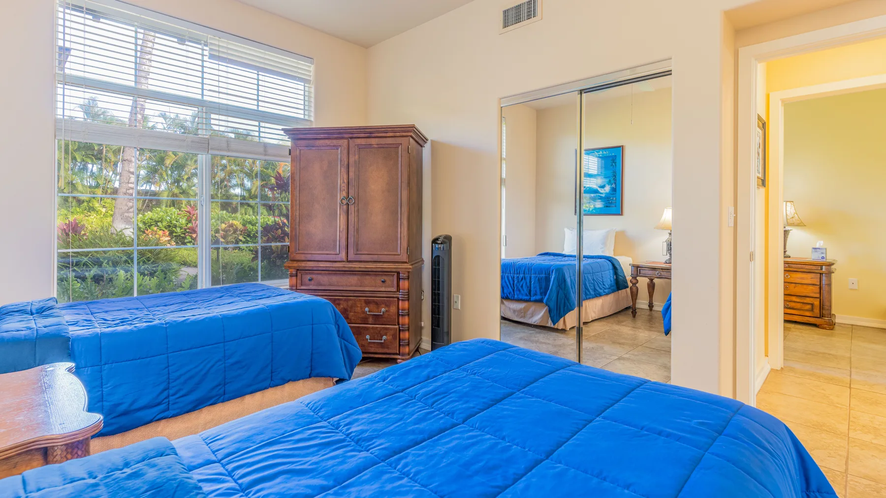 A bedroom with blue bedding, a large window, and mirrored closet doors.
