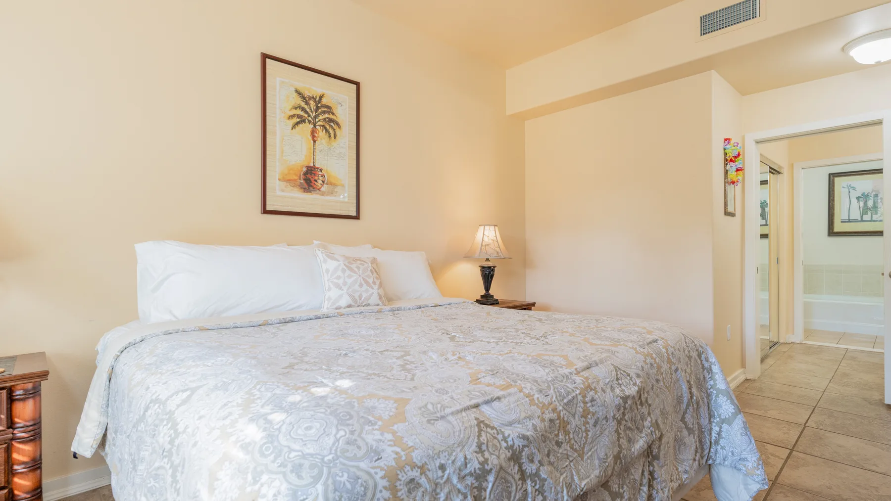 A bedroom with a large bed, framed artwork, and a doorway to the adjoining area.