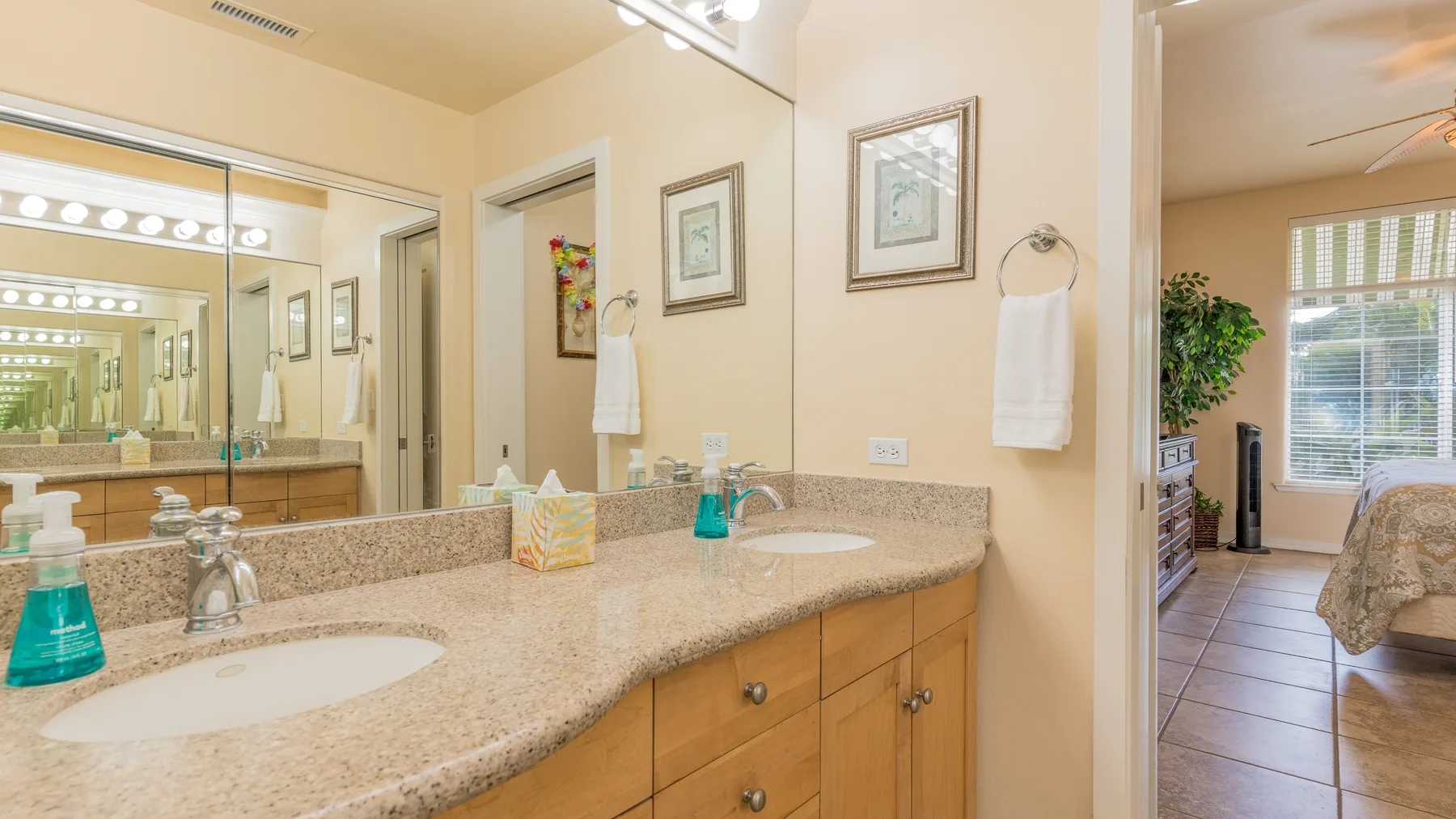 A bathroom vanity with a wide mirror and a doorway opening onto a bedroom.