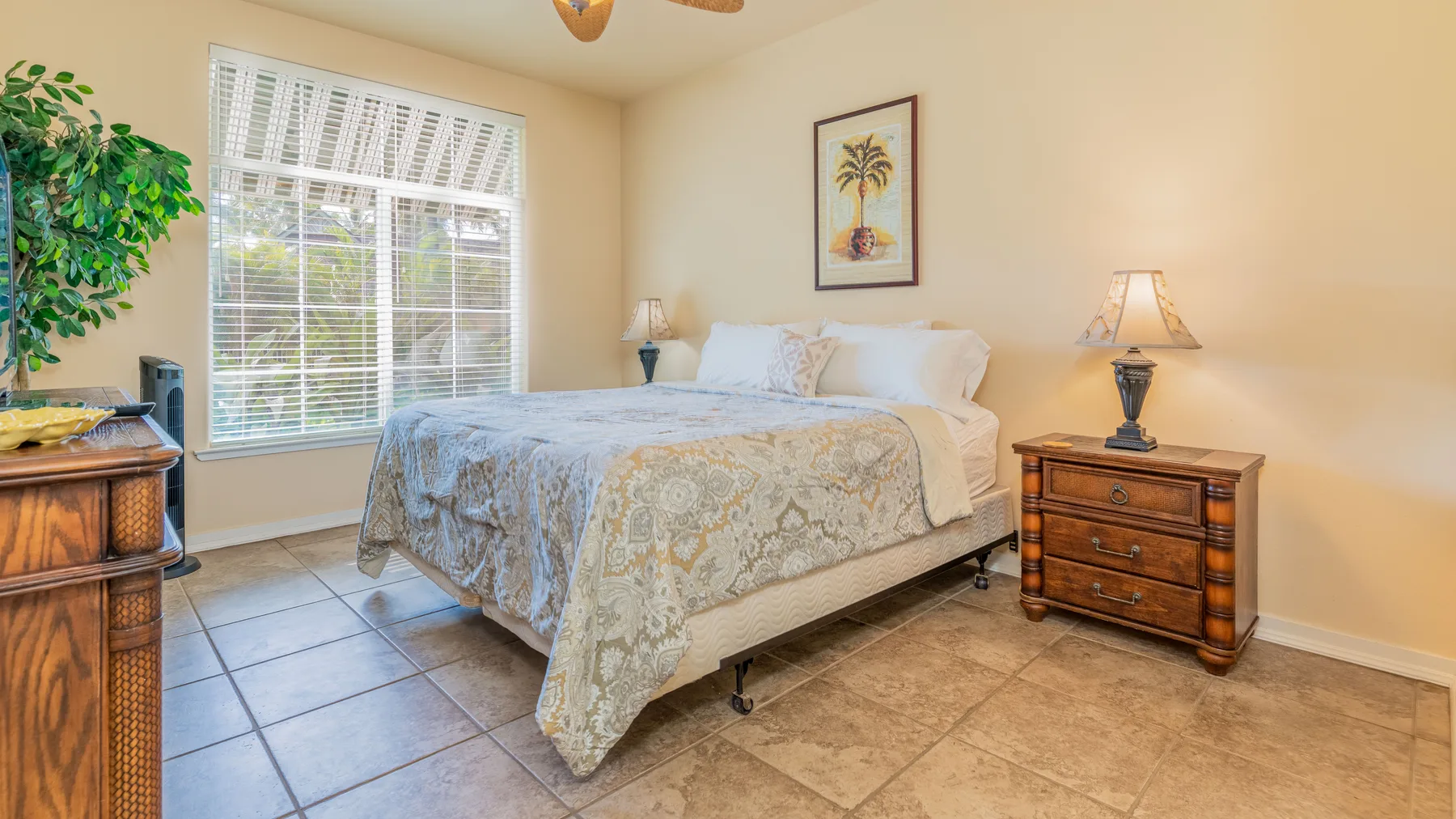 A bedroom with a bed beside a large window and wooden bedside tables.