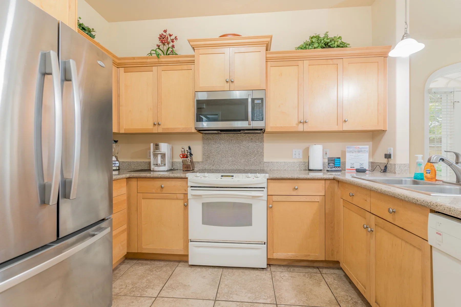 A bright kitchen with wooden cabinets, stainless steel appliances, and tiled flooring.