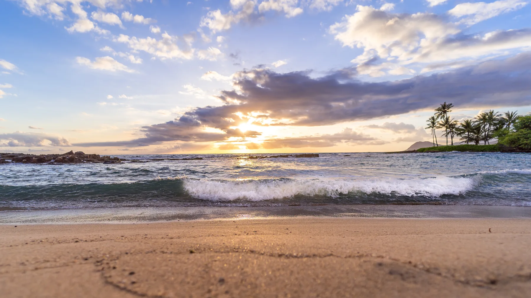 A sandy beach with ocean waves beneath a colorful sunset sky.