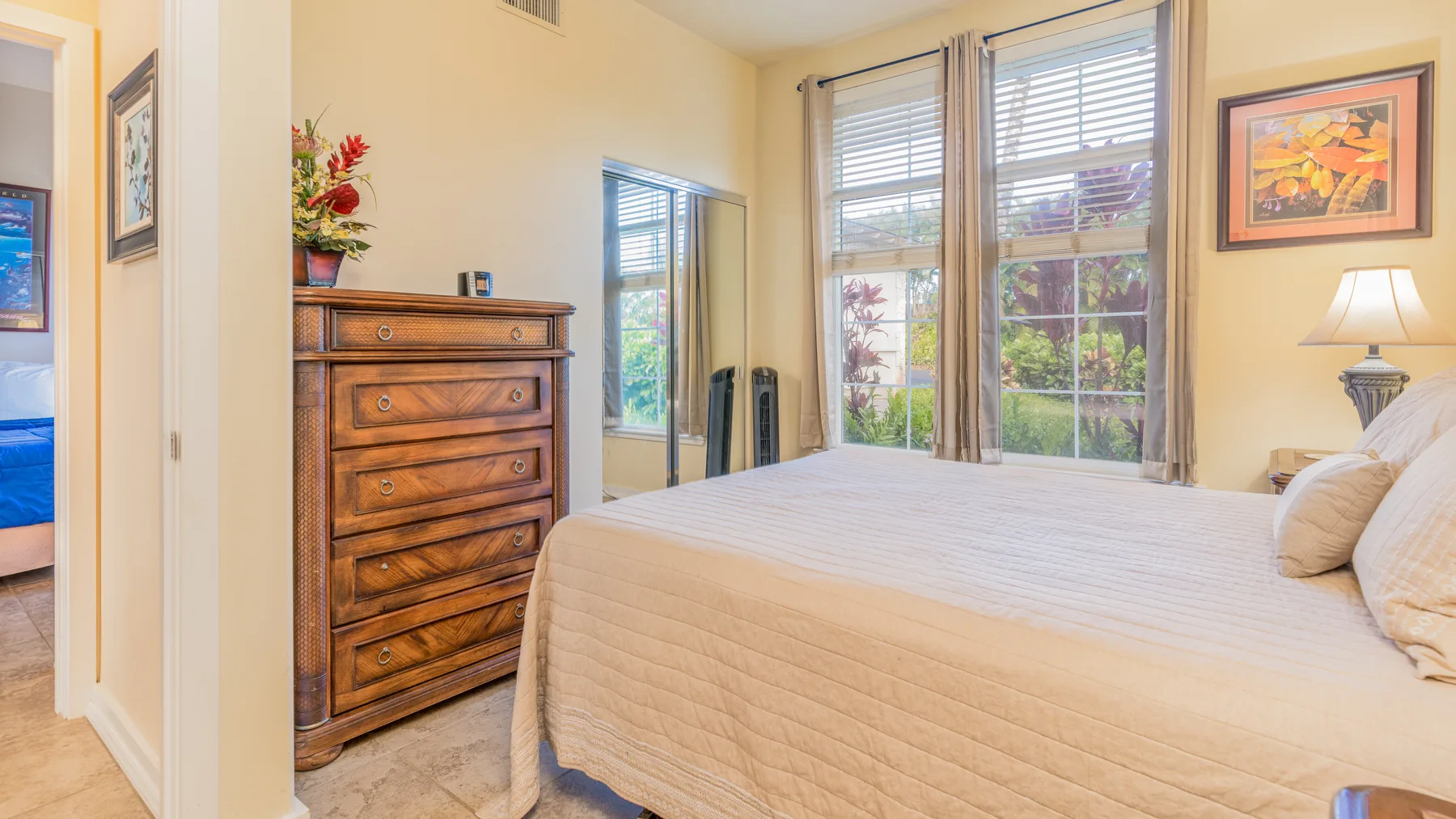 A bedroom with a neatly made bed beside tall windows.