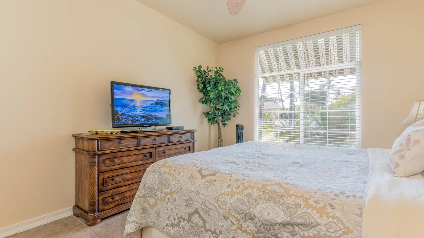 A bedroom with a bed, dresser, television, and a bright window.