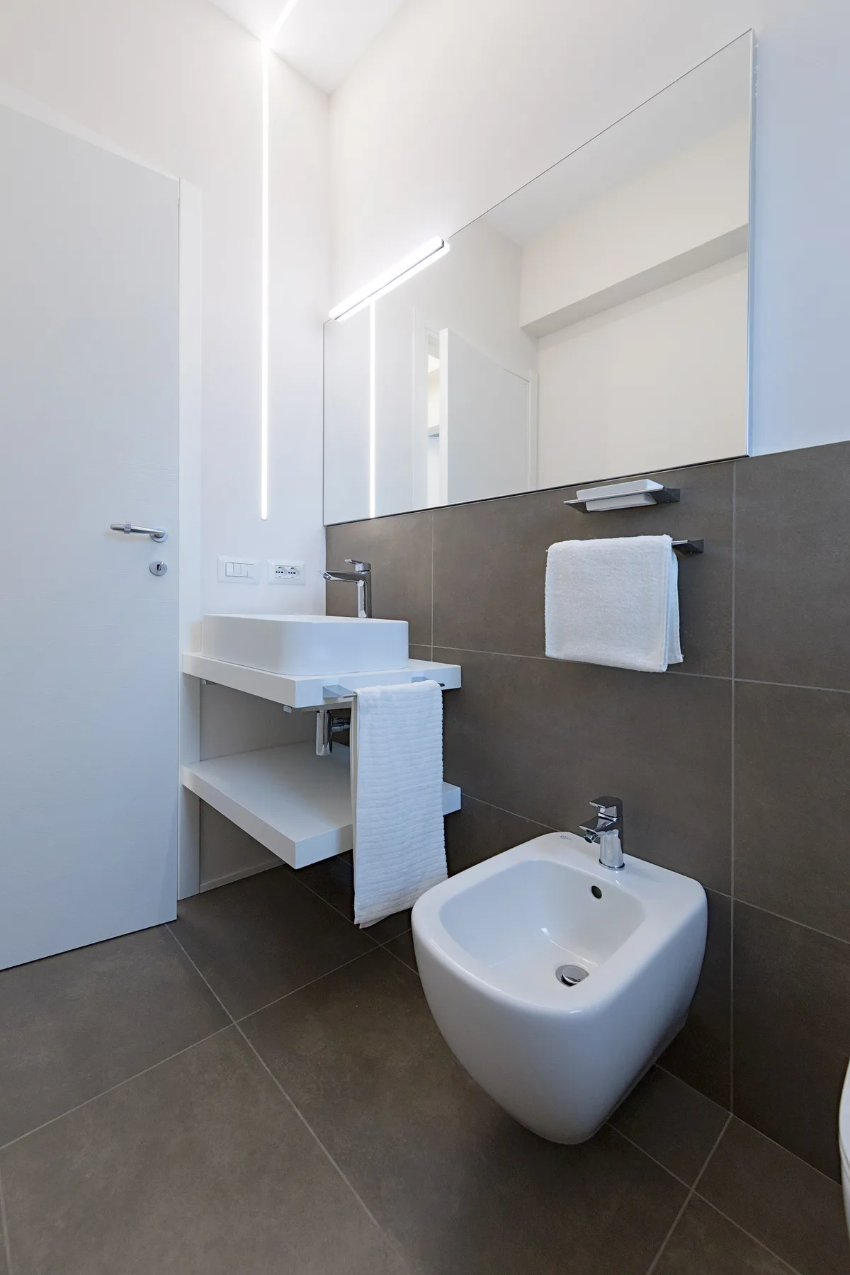 A modern bathroom with a wall-mounted sink, mirror, and bidet.