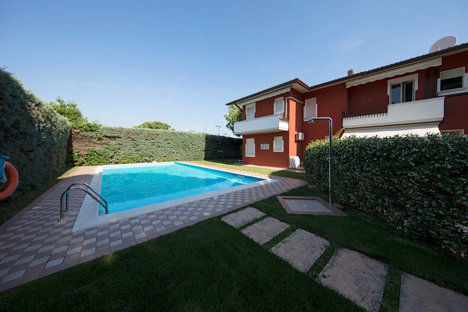 A swimming pool beside a red residential building and a paved patio.
