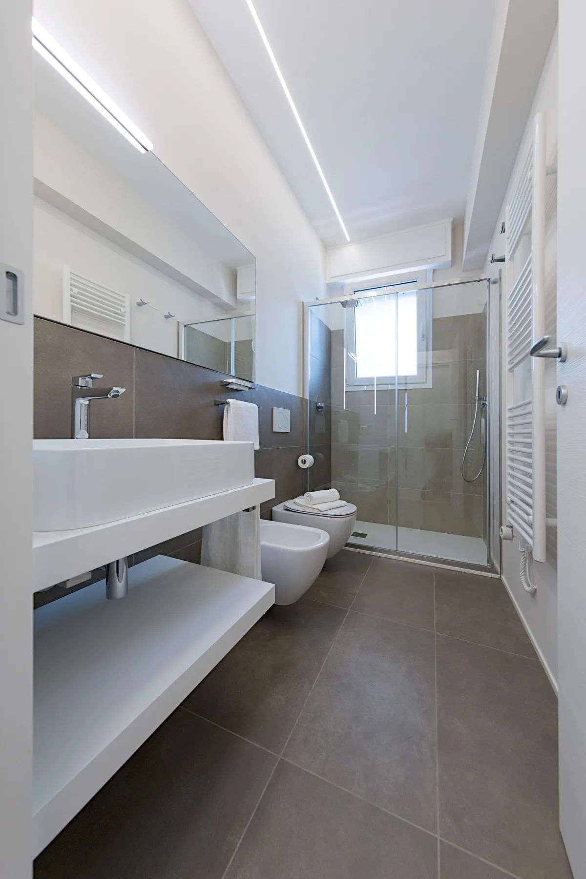 A modern bathroom with a long sink counter and a glass shower.