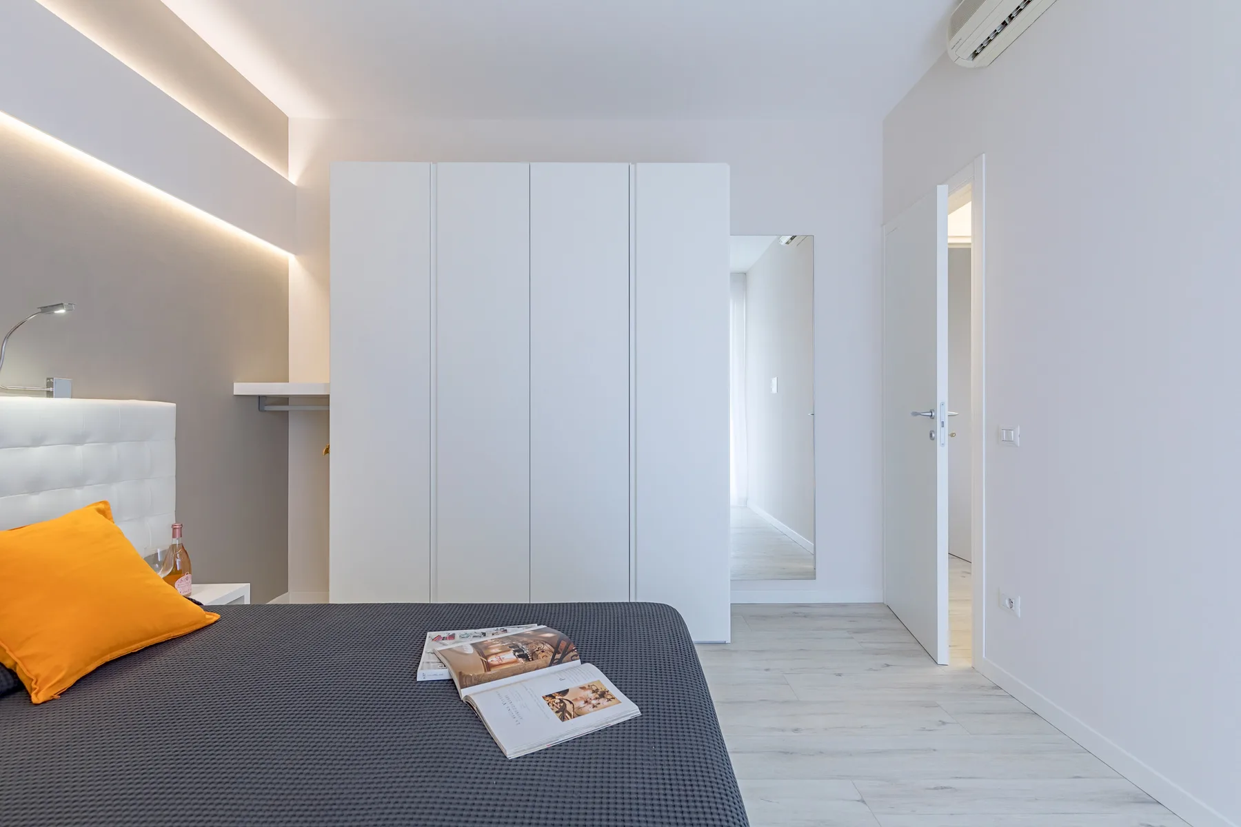 A bright bedroom with a bed, white wardrobe, and doorway opening onto a hall.