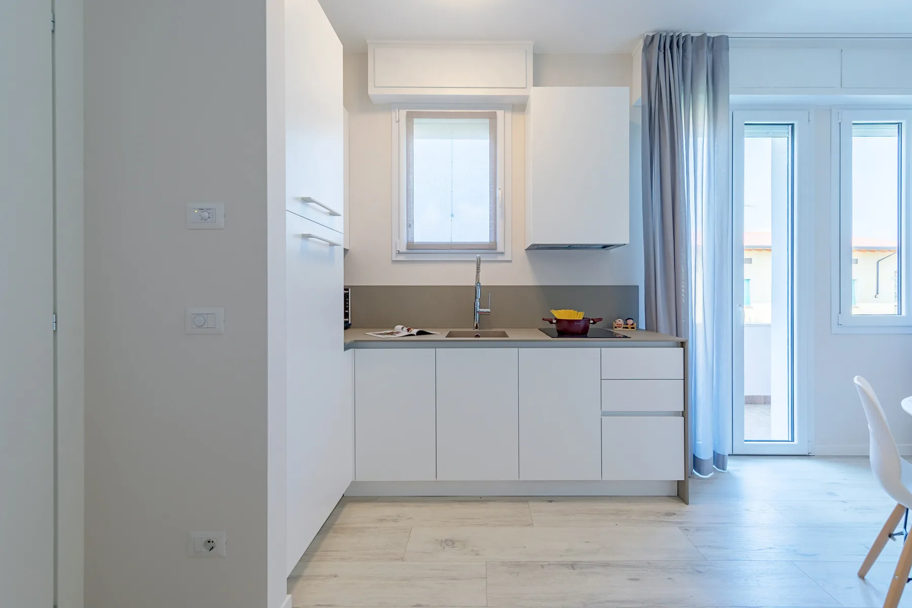 A bright kitchen with white cabinets and a counter beside tall windows.