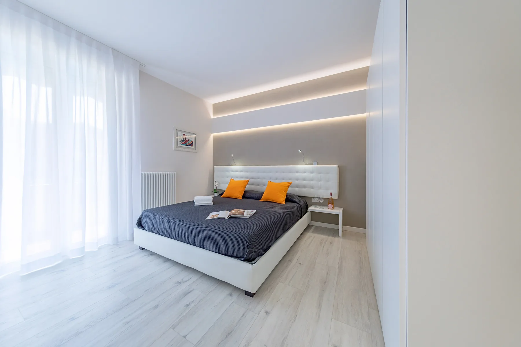A modern bedroom with a bed, orange accent pillows, and sheer curtains.
