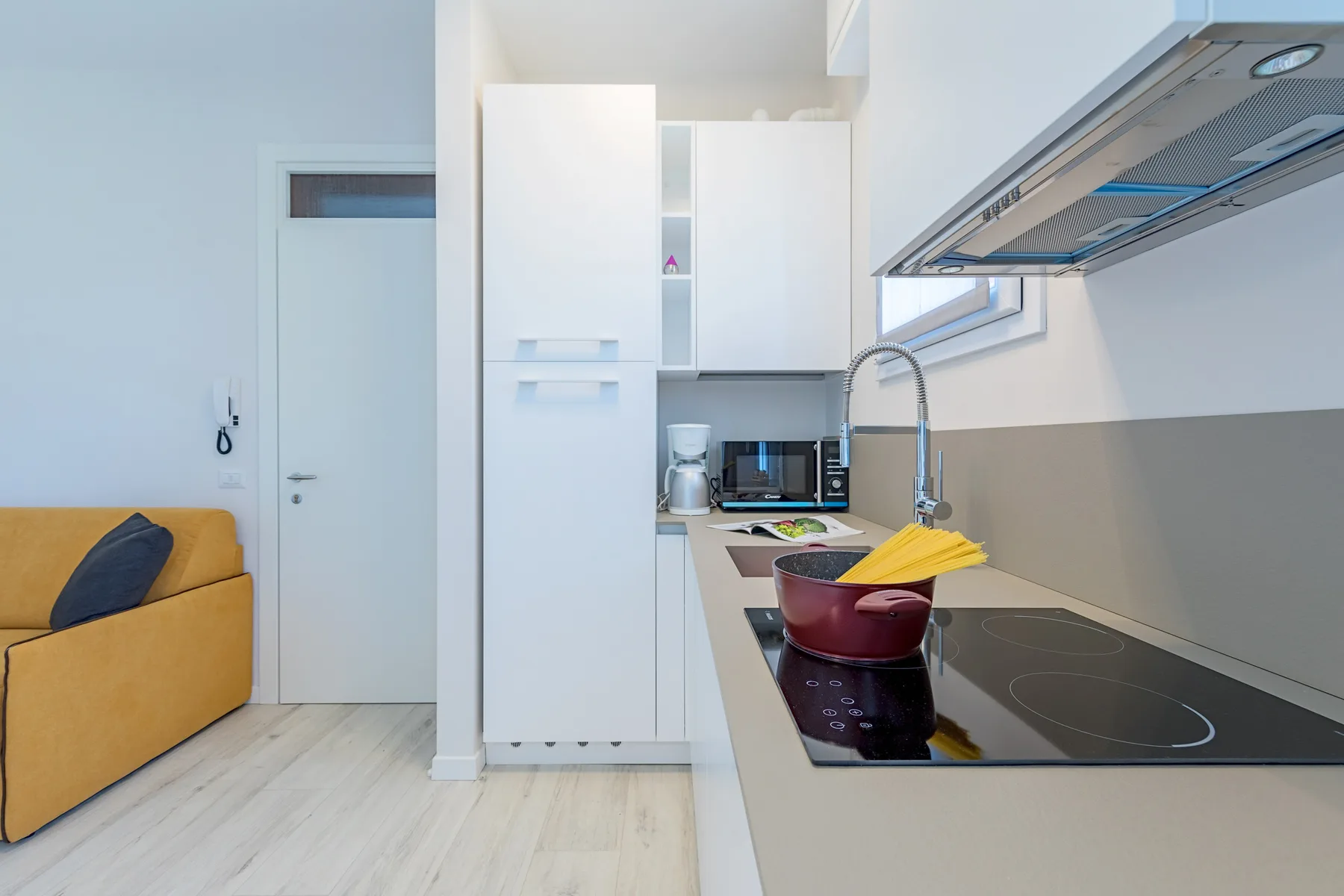 A compact kitchen with a cooktop, sink, and mustard-colored seating.
