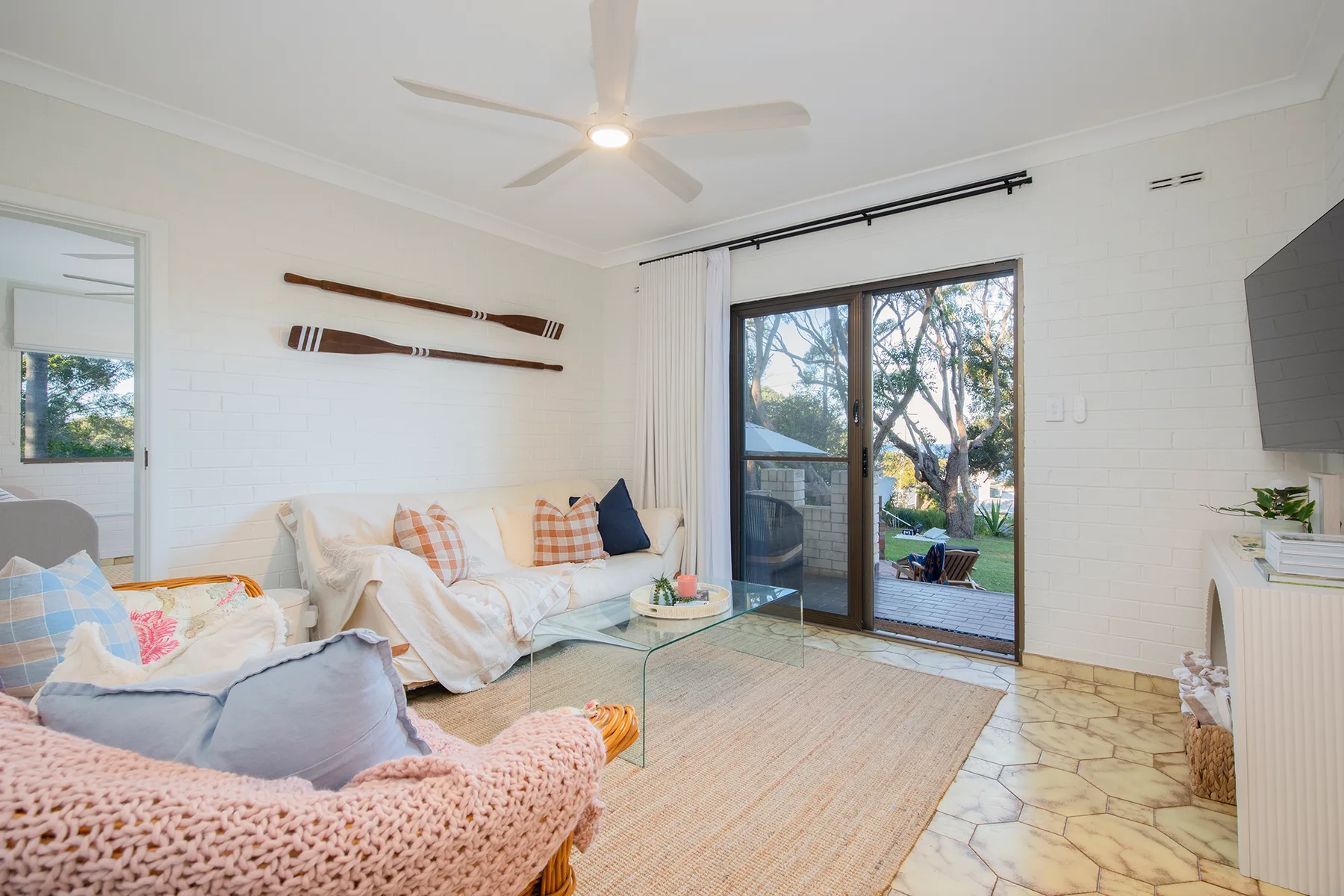 Sink into the generous living area seating with a book or favourite film, surrounded by soft coastal comfort and glimpses of greenery beyond.