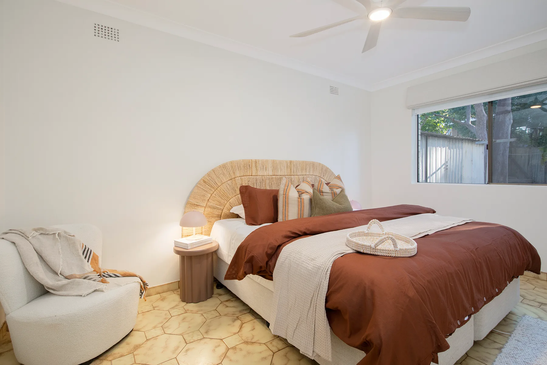 A bedroom with a bed, woven headboard, and a window overlooking greenery.