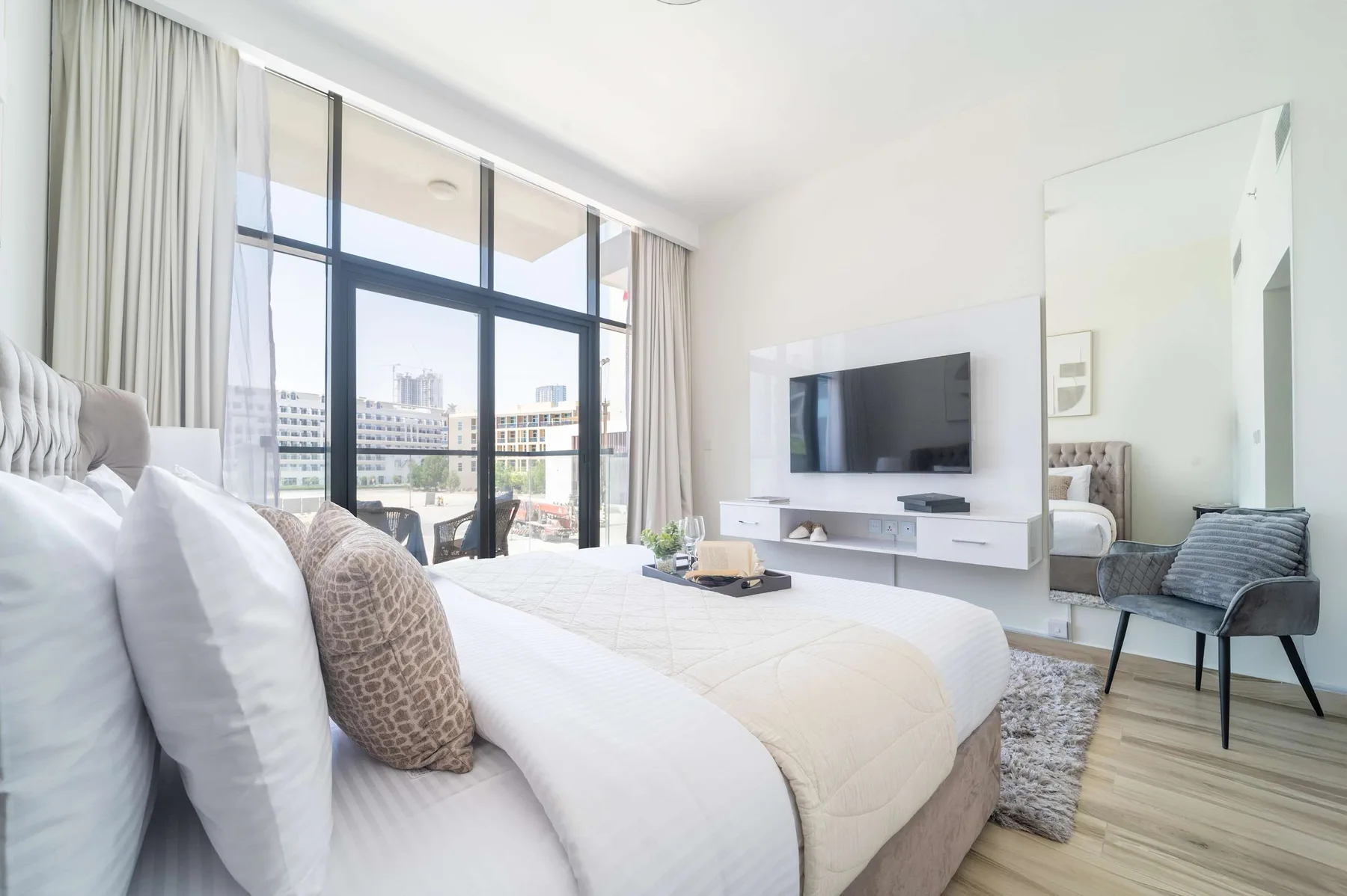 Un dormitorio luminoso con una cama tendida y un televisor en la pared.