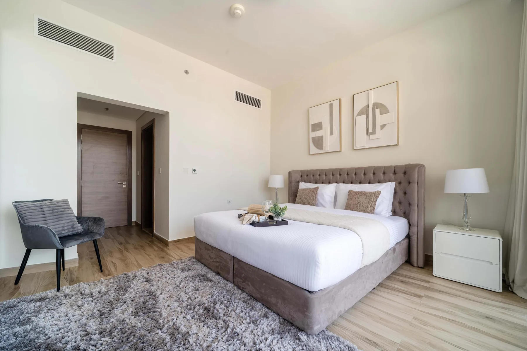 Un dormitorio luminoso con una cama, mesitas de noche y una alfombra gris.