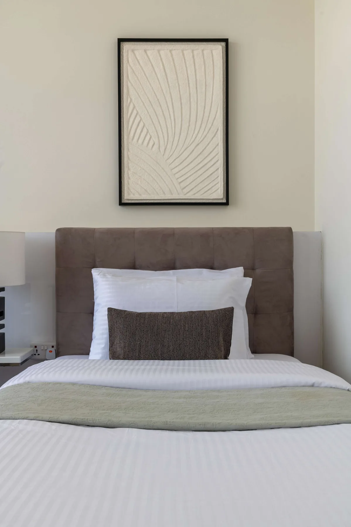 Una cama bien arreglada con ropa de cama blanca y un cuadro sobre el cabecero.