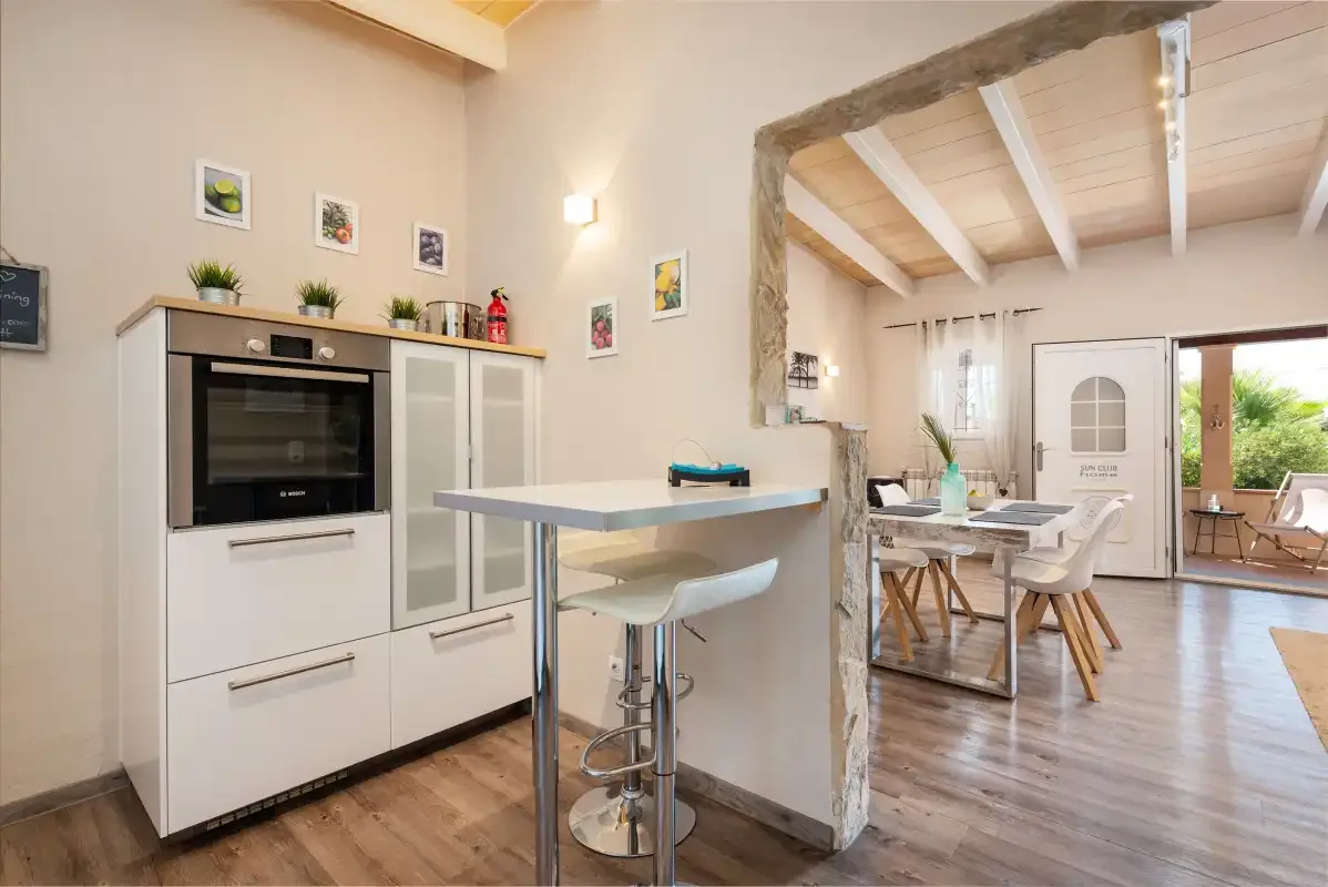 A bright kitchen opens into a dining area with a table and chairs.