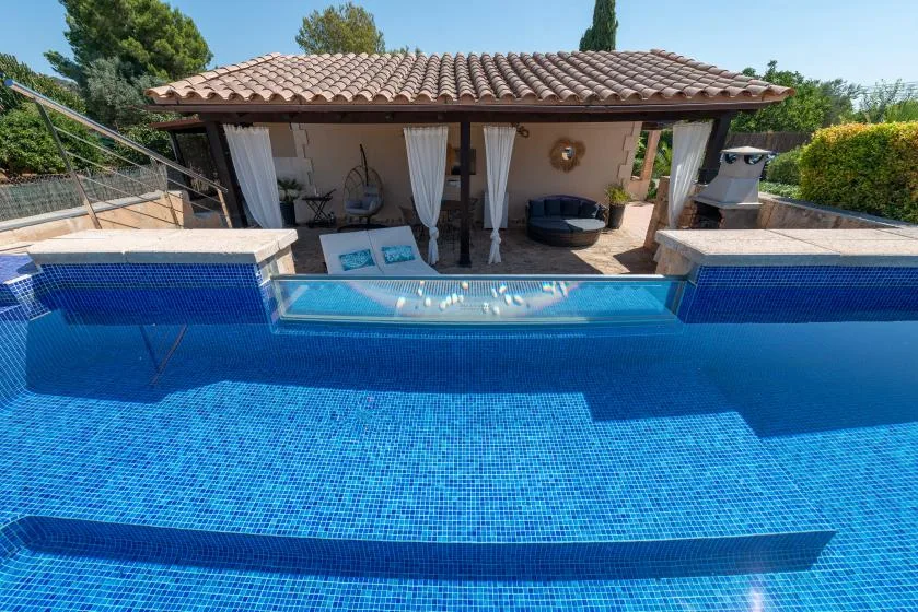 An outdoor swimming pool sits in front of a shaded patio with seating.
