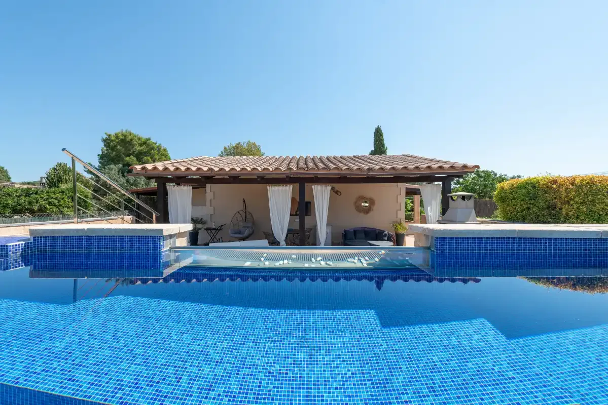A swimming pool in front of a covered patio with seating.