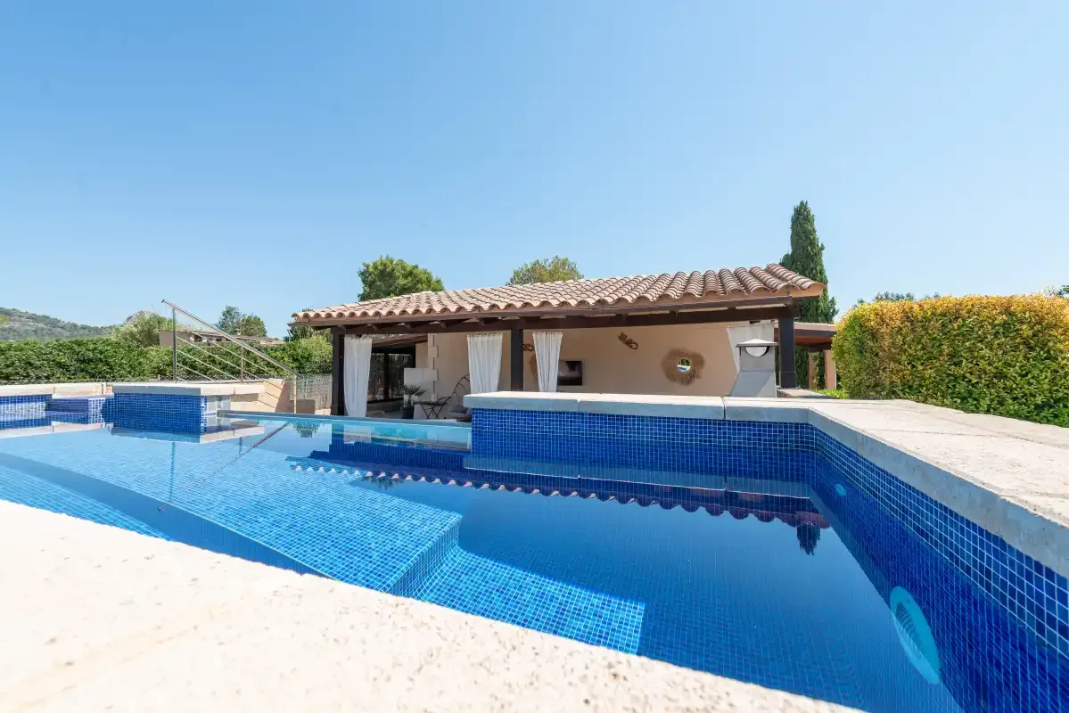 An outdoor swimming pool sits in front of a covered patio.