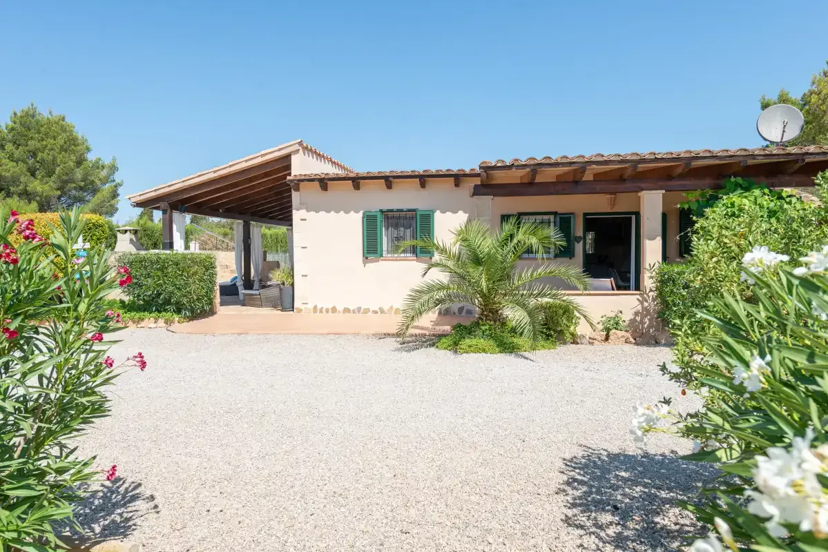 A single-story house faces a gravel courtyard, with plants along the edges.
