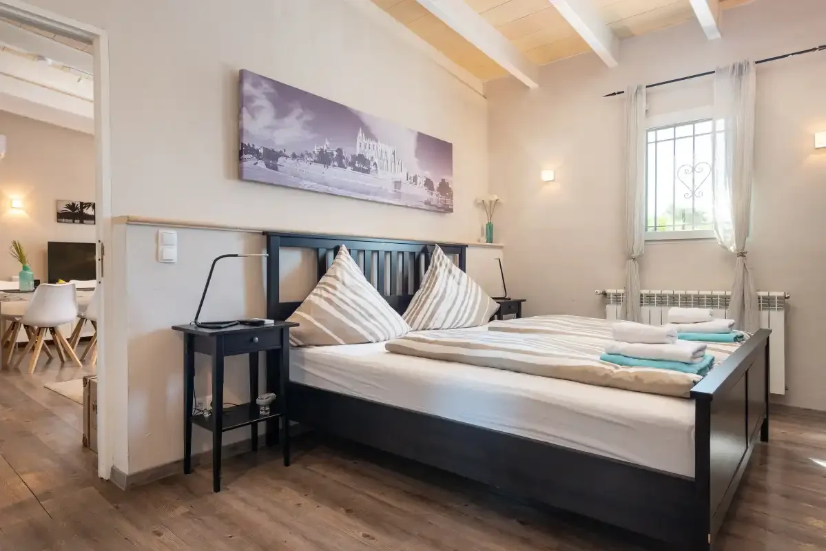 A bedroom with a bed, bedside table, and a window with sheer curtains.