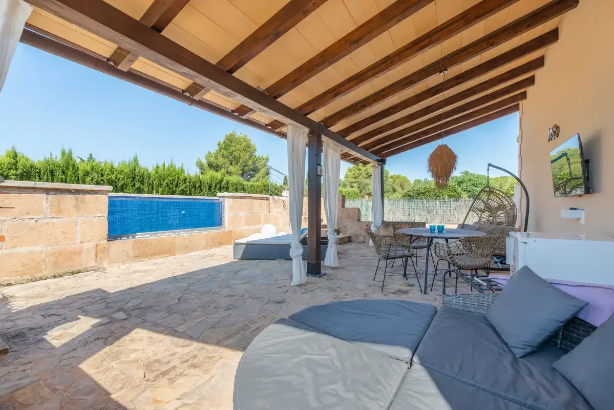 A covered outdoor patio with seating, a dining table, and a swimming pool.