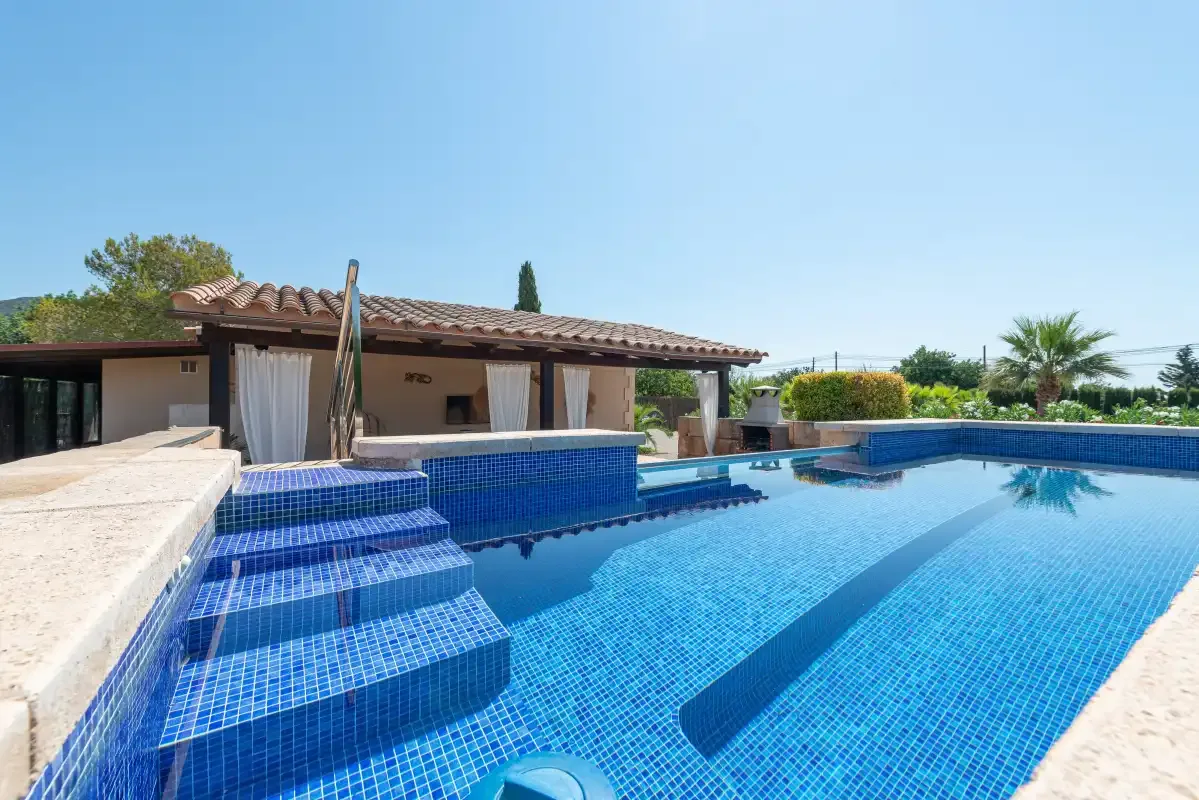 An outdoor swimming pool with blue-tiled steps beside a low building.