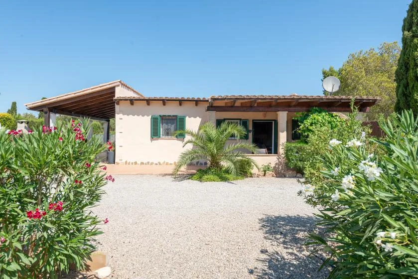 A single-story house faces a gravel yard bordered by flowering plants.