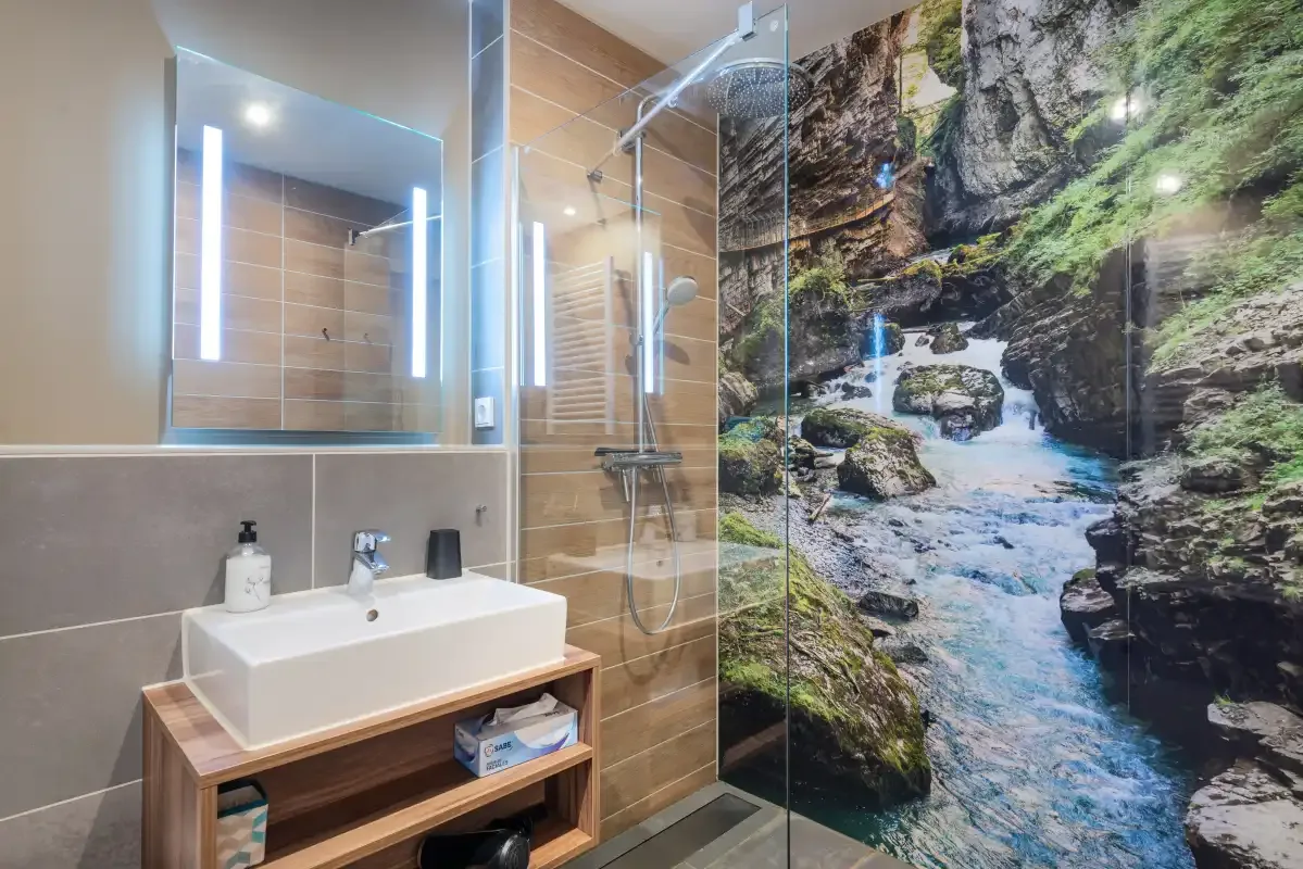 A modern bathroom with a sink and a glass shower beside a nature mural.
